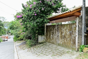 A residential area with a paved driveway leading to a gated entrance, a parked motorcycle, and a car on the street. - Jubarte Chalés | Confort near the beach (Ilhabela)
