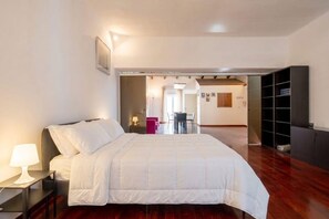 A hotel room with a bed, a desk with a lamp, a bookshelf, and a view of the hallway. - Murat Wooden House | Rustic Charm in Central Bari (Bari)