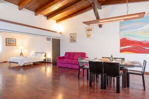 A spacious room with a wooden ceiling, a bed, a pink sofa, a dining table with chairs, and artwork on the walls. - Murat Wooden House | Rustic Charm in Central Bari (Bari)