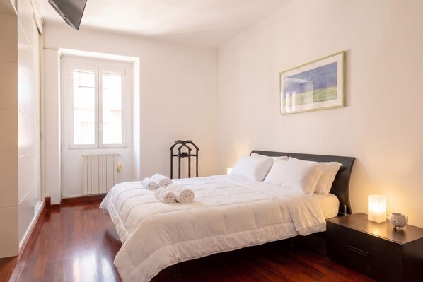 A bedroom with a bed, a nightstand, a radiator, a window, and a framed picture on the wall. - Murat Wooden House | Rustic Charm in Central Bari (Bari)