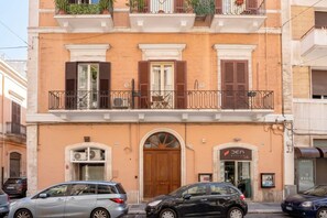 A multi-story building with a central entrance, balconies with plants, and parked cars on the street. - Murat Wooden House | Rustic Charm in Central Bari (Bari)