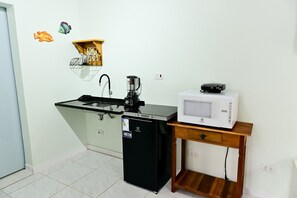 Eine kleine Küchenzeile mit Spüle, einem schwarzen Kühlschrank, einer Mikrowelle und einem Holztisch.