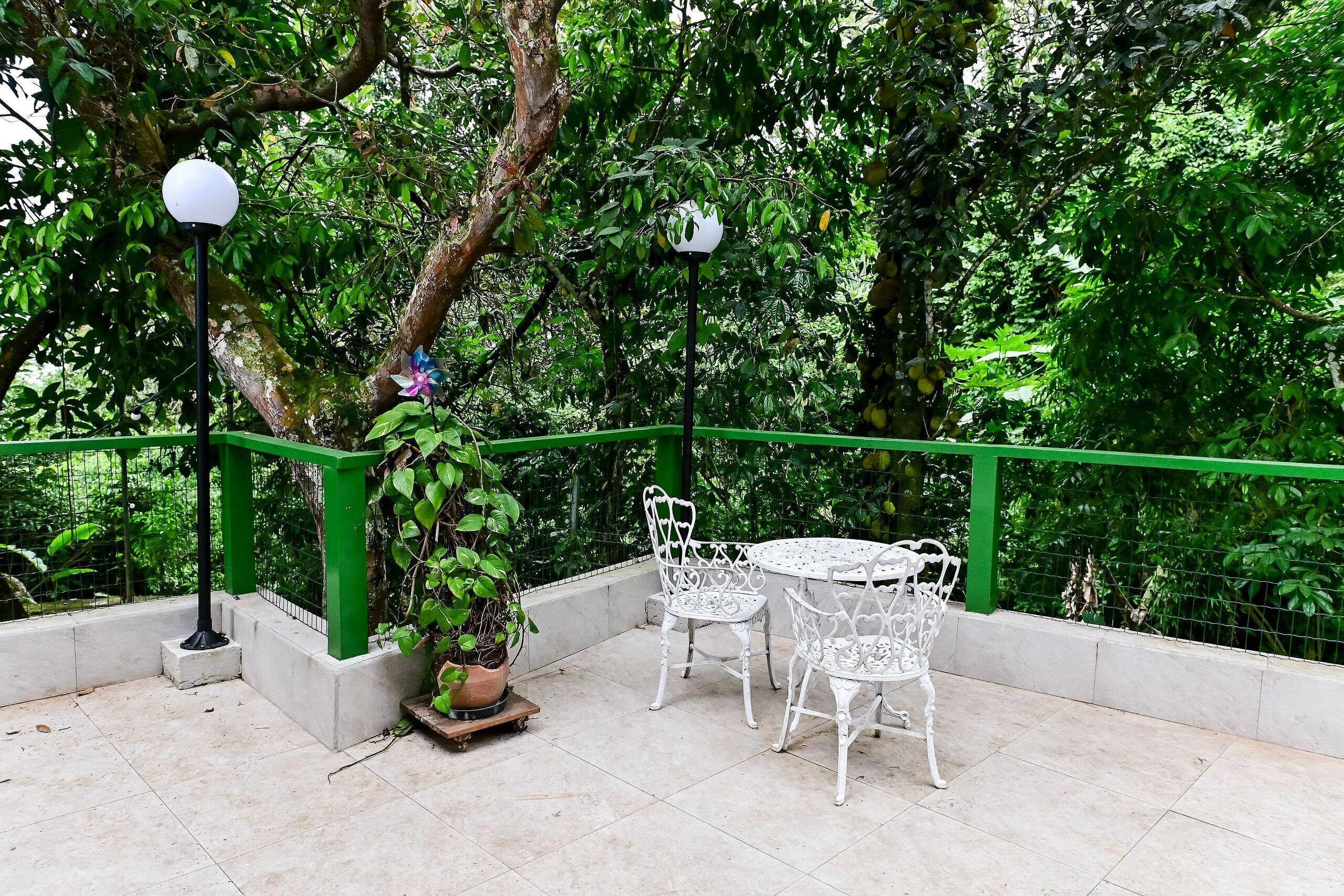 An outdoor seating area with white metal chairs and tables, surrounded by a green railing, and potted plants.
