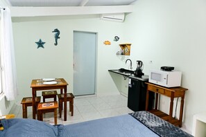 Ein kompakter Raum mit einem Bett, einem kleinen Esstisch, einer Küchenzeile mit Mikrowelle und einer Tür zu einem weiteren Zimmer.