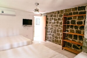 Ein Zimmer mit zwei Betten, einem Fernseher, einem Deckenventilator und einer Steinwand.