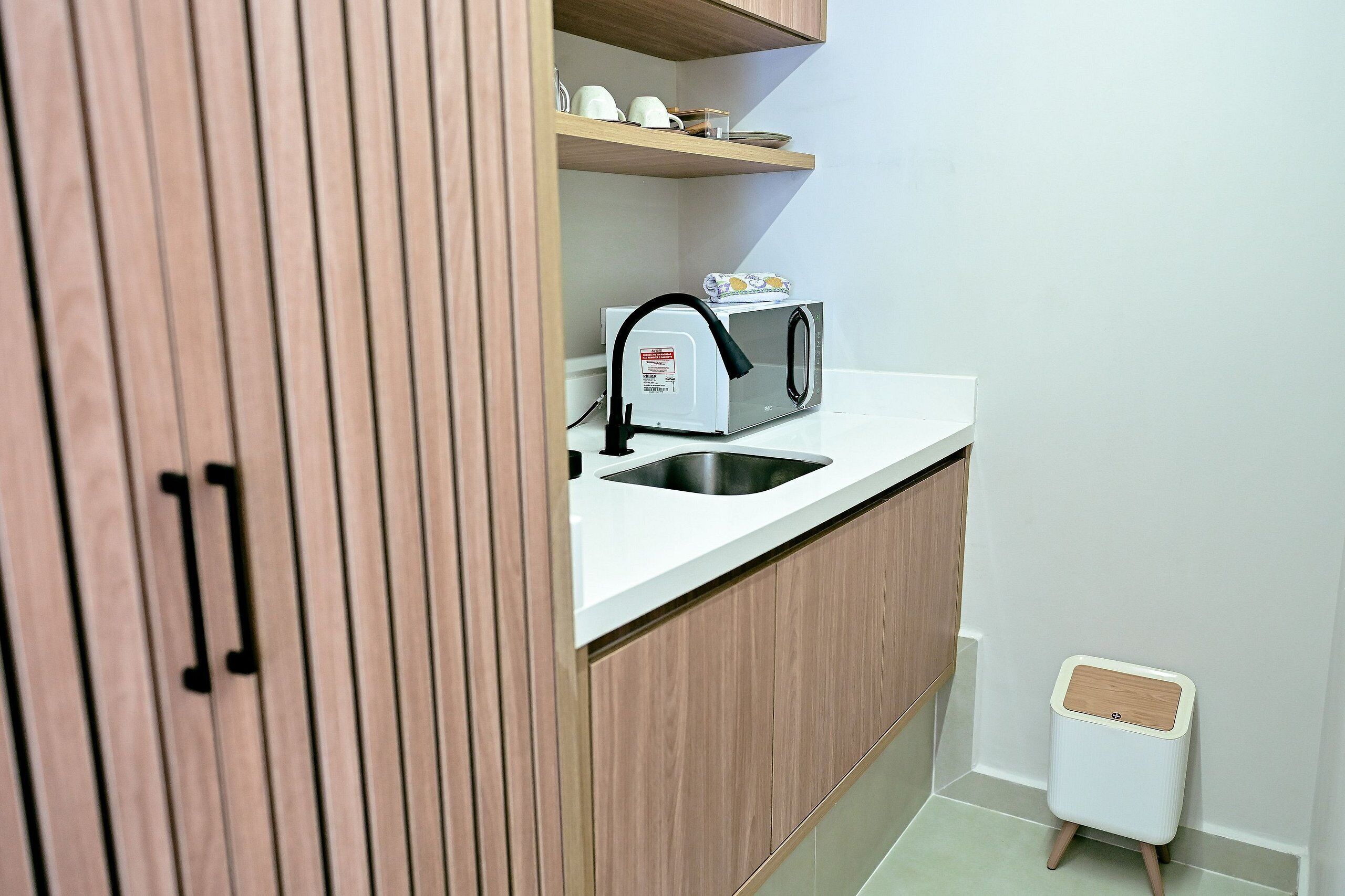 A compact kitchenette with a built-in microwave, a sink, and a small trash bin.