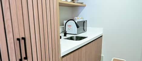 A compact kitchenette with a built-in microwave, a sink, and a small trash bin.