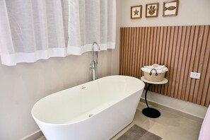A modern bathroom with a freestanding bathtub, a towel rack with a basket, and a wooden panel wall. - Studio Bonete | Bathtub and an incredible breakfast (Ilhabela)