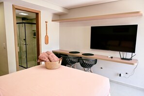 A modern bedroom with a bed, a TV mounted on the wall, and a shower area.