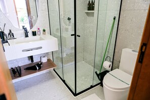 A modern bathroom with a glass-enclosed shower, a white sink with a mirror, and a toilet.