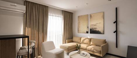 A modern living room with a sofa, armchair, coffee table, and a dining area with a bar.