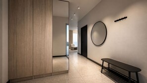 Un interior moderno con un panel de madera, una banca, un espejo redondo y una puerta que da a otra habitación.