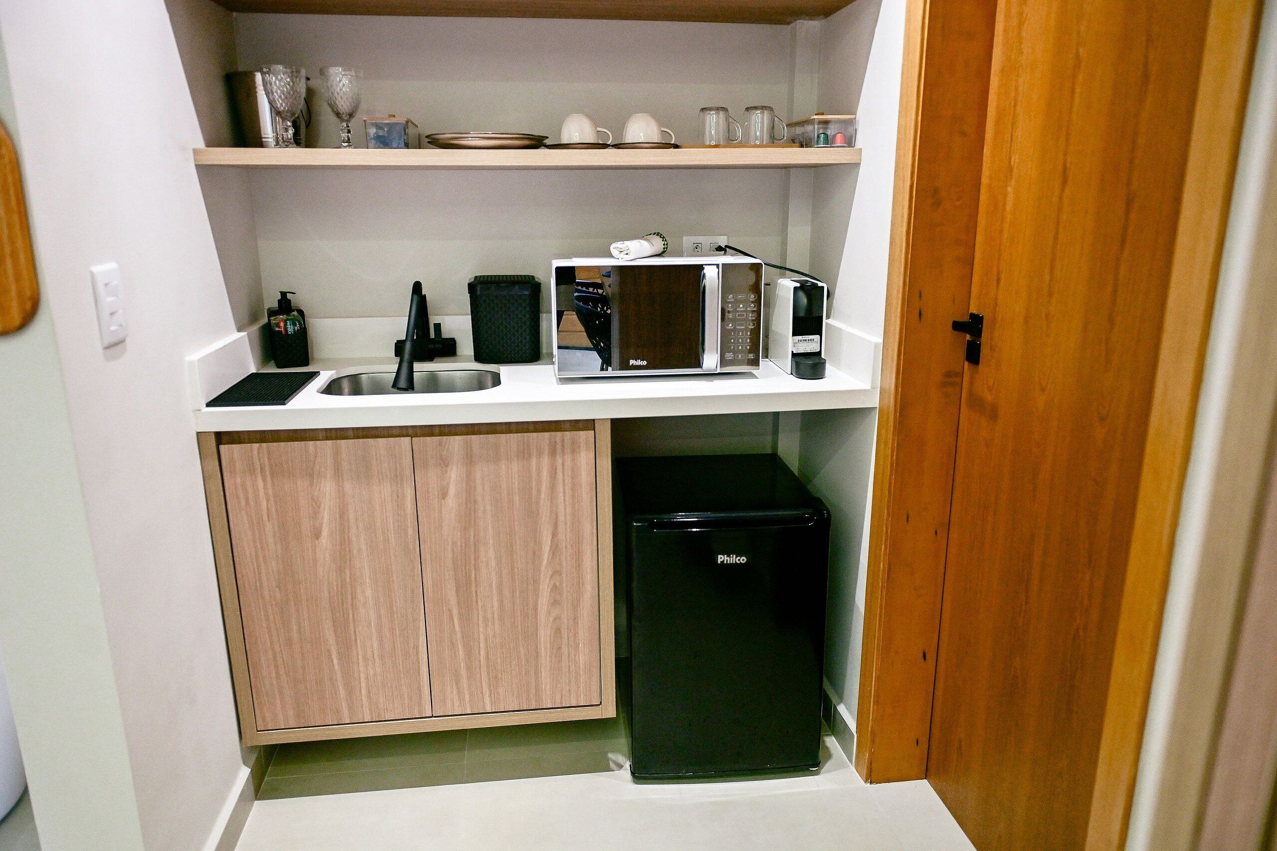 A compact kitchen with a sink, a microwave, a small refrigerator, and a cabinet.