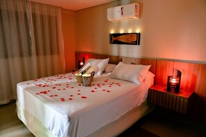 A hotel room with a bed, bedside tables, a wall-mounted air conditioner, and a wall art piece. - Studio Viana | Luxury studio with bathtub (Ilhabela)