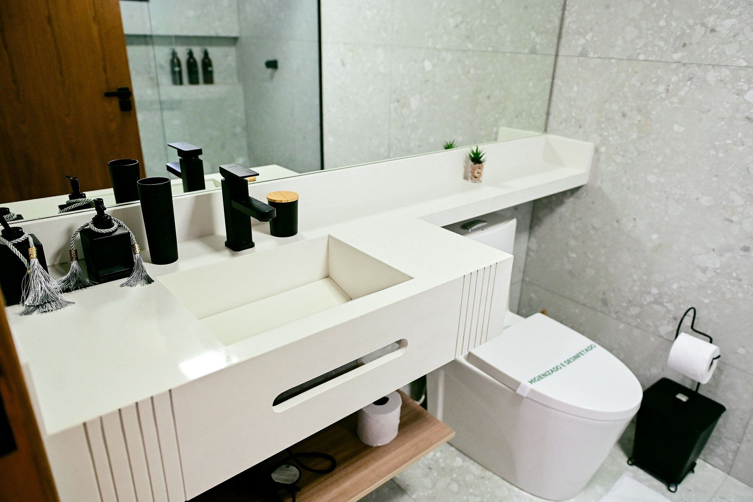 Une salle de bain moderne avec un meuble-lavabo blanc, un miroir, un évier, des toilettes et une poubelle.