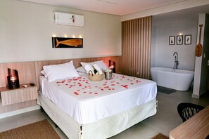 A hotel room with a bed, bedside table, lamp, and a bathtub.