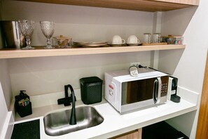 A kitchenette with a microwave, sink, and various kitchenware on shelves.