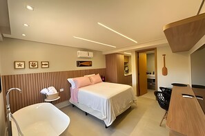 A modern hotel room with a bed, a white bathtub, a wooden desk, and a bathroom with a shower.