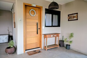 A wooden door with a nameplate, a wicker pendant light, a small wooden table, and potted plants.