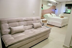 A modern living room with a beige sofa, a white bed, and a small side table with a basket.