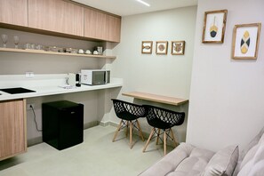A compact kitchenette with a microwave, a small black refrigerator, and a wooden cabinet. There are two black chairs and a small table.