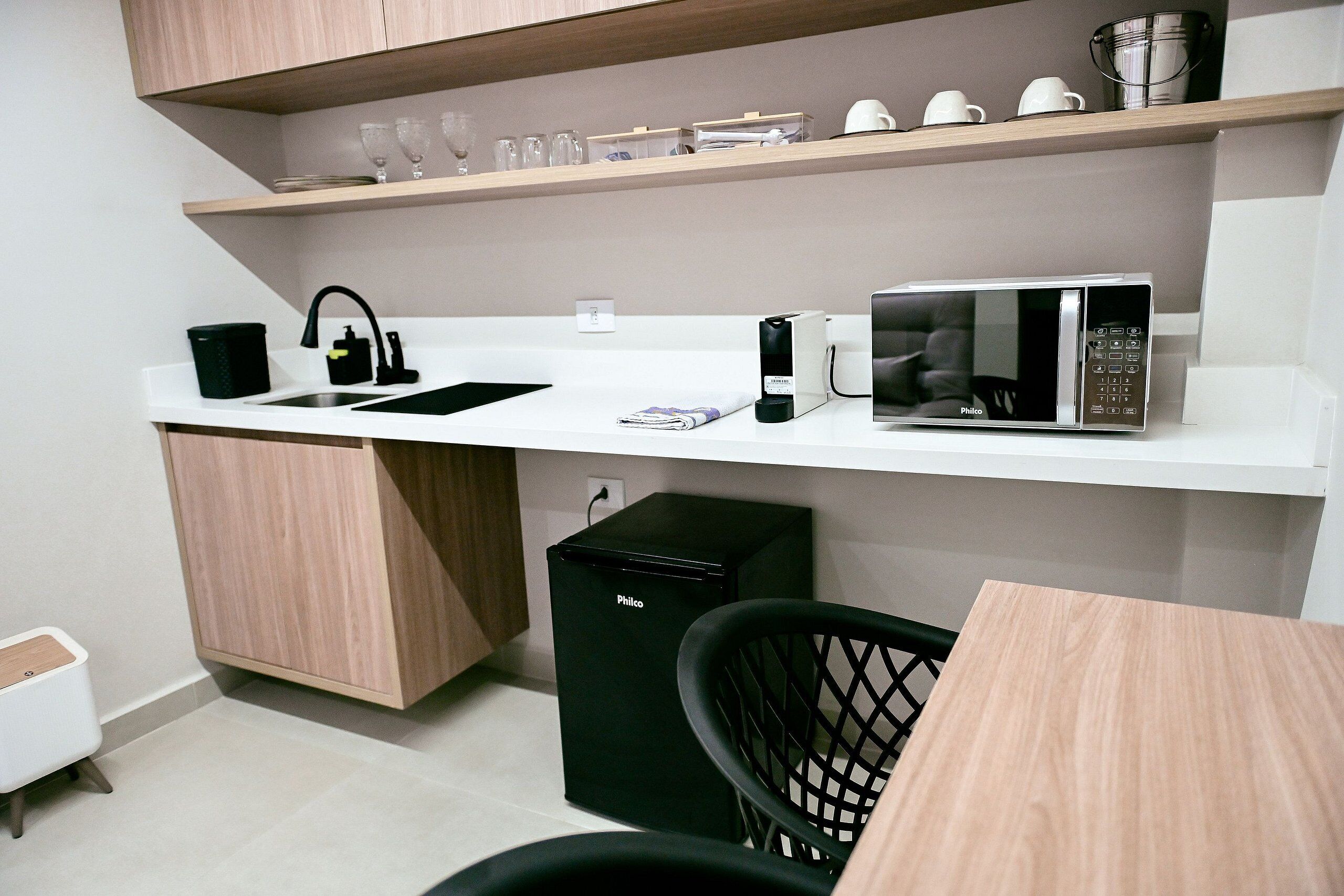 A compact kitchenette with a white countertop, a black coffee maker, a microwave, and a black trash bin.