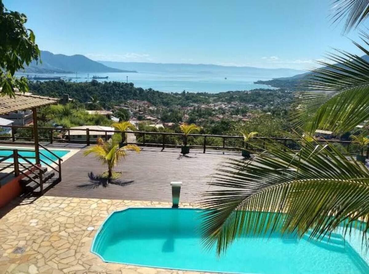 A pool area with a view of the sea and mountains, surrounded by palm trees and a wooden deck.