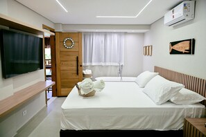 A hotel room with a bed, a television, a shower, and a wall-mounted air conditioner.