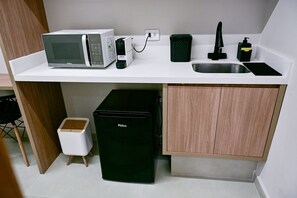 A compact kitchenette with a microwave, a small refrigerator, a sink, and a trash bin.
