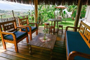 A wooden deck with outdoor furniture, including chairs and a table, surrounded by lush greenery and a view of the landscape.
