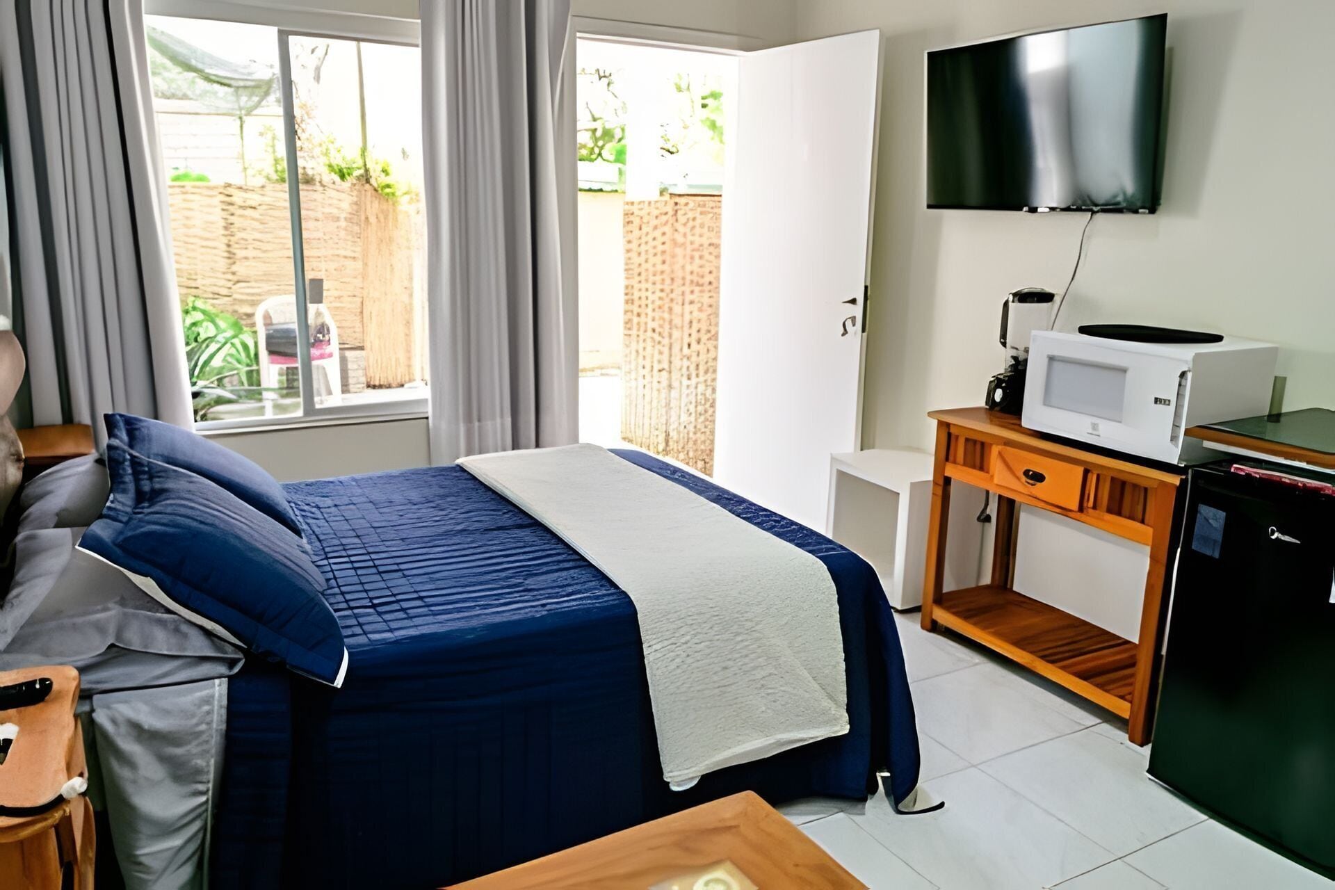 Ein Hotelzimmer mit Bett, einem an der Wand befestigten Fernseher, einer Mikrowelle auf einem Holztisch und Blick ins Freie.