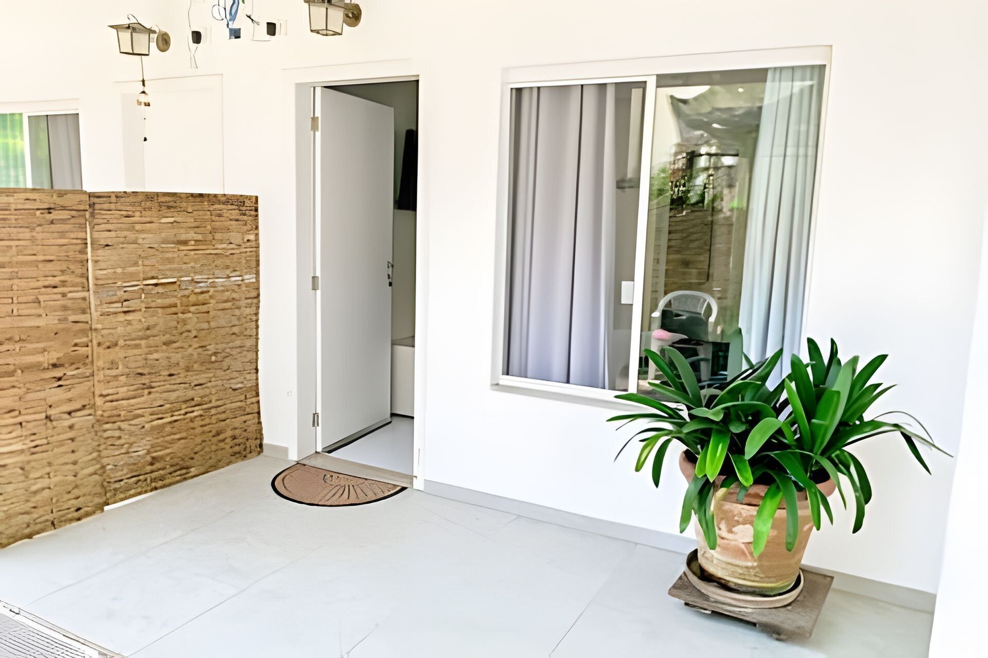 A modern interior with a white wall, a wooden partition, a potted plant, and a door leading to another room.