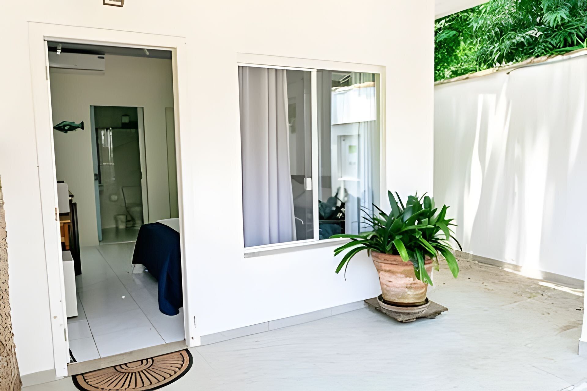 A doorway leading to a room with a bed, a potted plant, and a window with curtains.