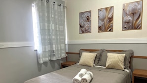 A neatly made bed with a patterned bedspread, two pillows, and rolled towels on a wooden nightstand. - 403 Apto Versátil e Aconchegante (Belém)