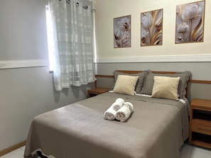 A neatly made bed with a patterned bedspread, two pillows, and rolled towels on a wooden nightstand. - 403 Apto Versátil e Aconchegante (Belém)