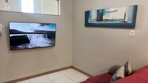 Un saló amb un televisió de pantalla plana penjada a la paret, un sofà amb coixins i un quadre sobre la televisió.