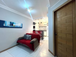 Una sala de estar moderna con un sofá rojo, una cocina al fondo y una puerta de madera.