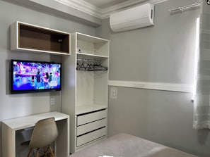 A room with a TV mounted on the wall, a desk with a chair, a wardrobe with hanging space, and an air conditioning unit. - 403 Apto Versátil e Aconchegante (Belém)