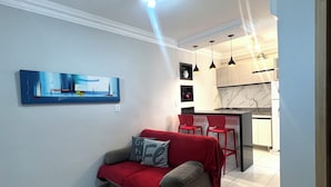 A modern living room with a sofa, a red throw blanket, and a painting on the wall. - 403 Apto Versátil e Aconchegante (Belém)