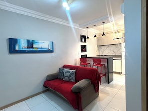 A modern living room with a sofa, a red throw blanket, and a painting on the wall. - 403 Apto Versátil e Aconchegante (Belém)