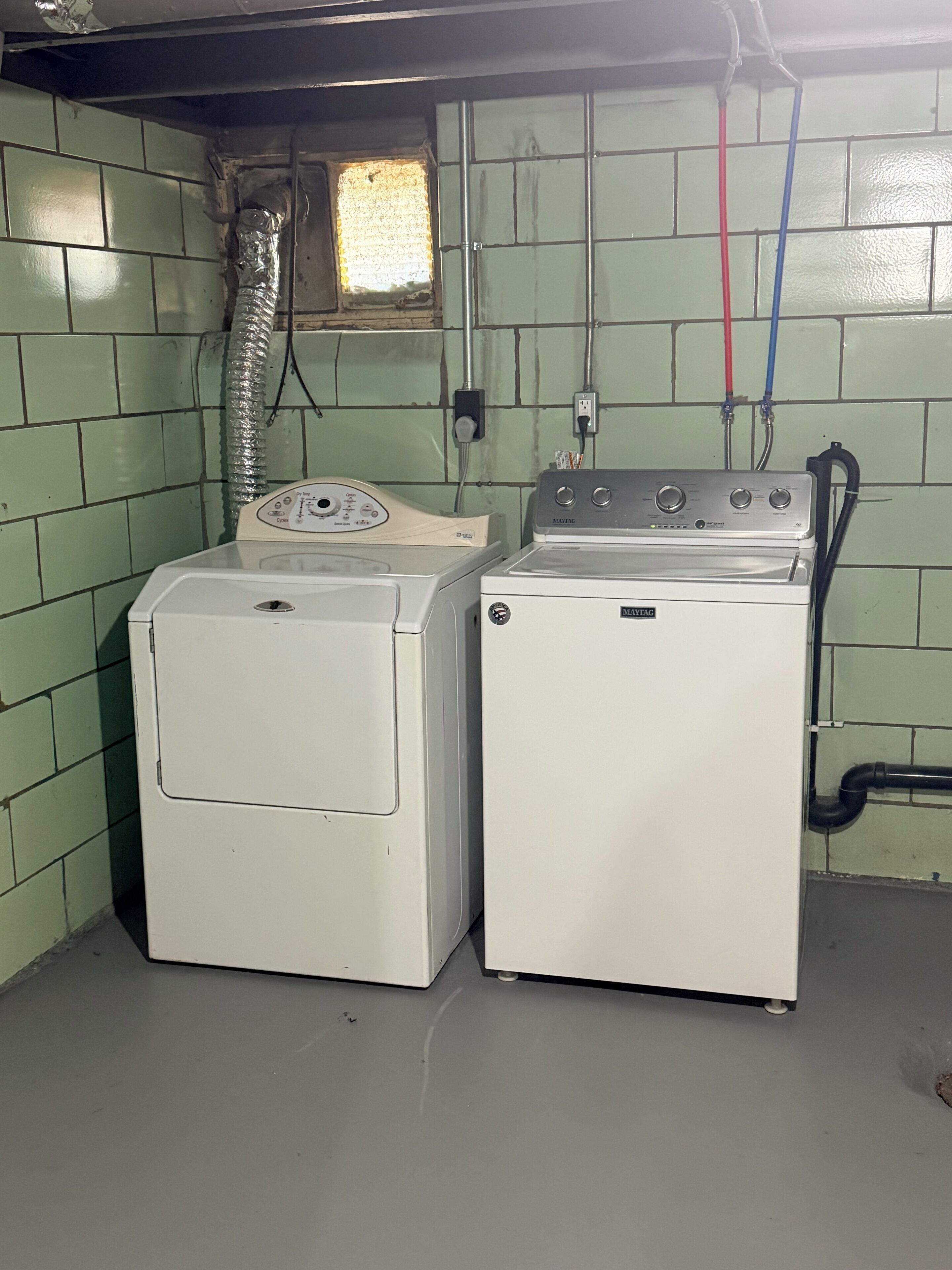 A laundry room with two stacked washers and dryers, a window with a view, and visible plumbing.