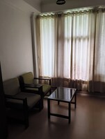Una habitación con sofá, una mesita y ventana con cortinas.