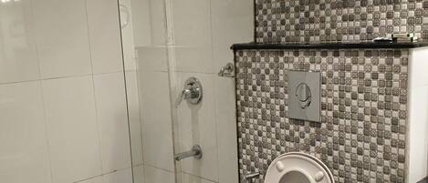Un baño con inodoro, ducha y pared con azulejos.