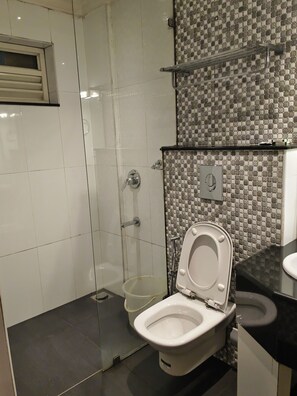 A bathroom with a toilet, a shower, and a tiled wall. - Matha Residency Munnar (Devikolam)