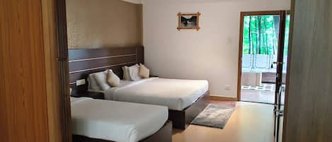 A hotel room with two beds, a ceiling fan, a small picture on the wall, and a view of greenery outside.