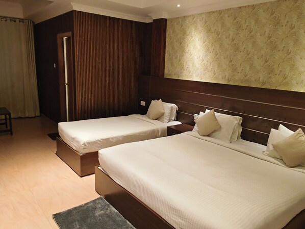 A hotel room with two beds, a wooden headboard, a patterned wall, and a small stool.