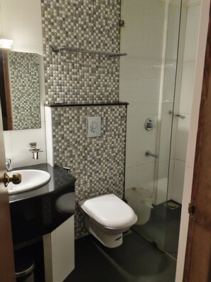 Un baño con pared de azulejos, lavamanos, inodoro y zona de ducha.