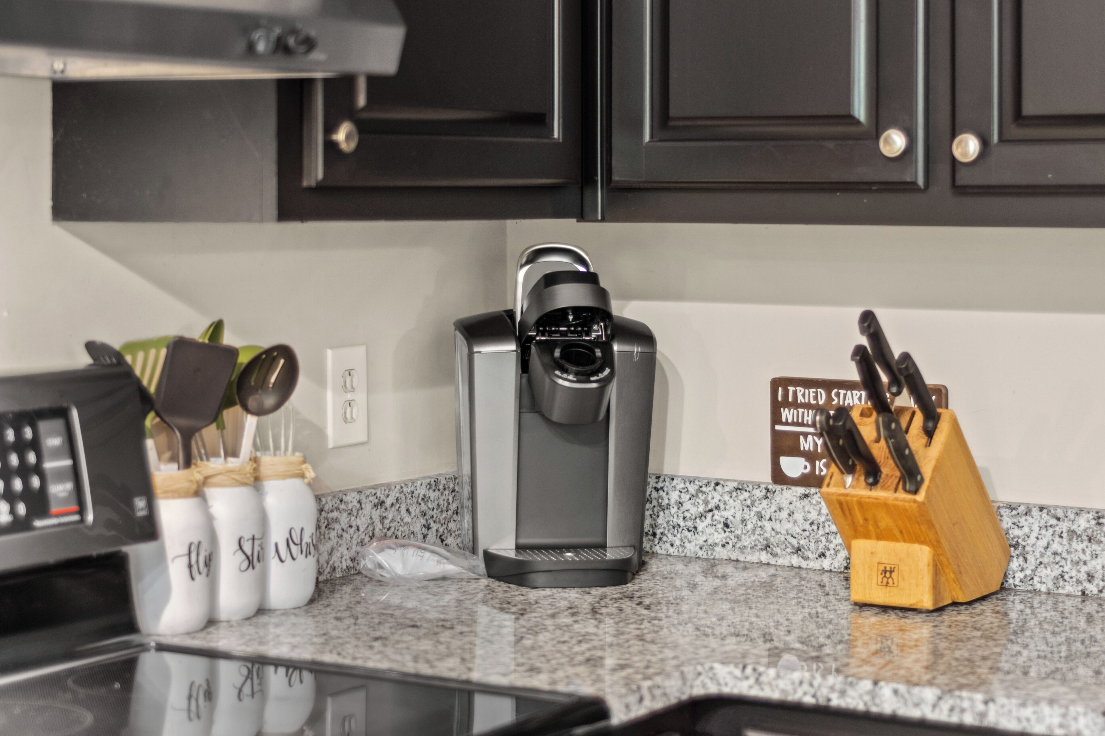 A kitchen with a coffee maker, a knife block, and a sign on the wall.