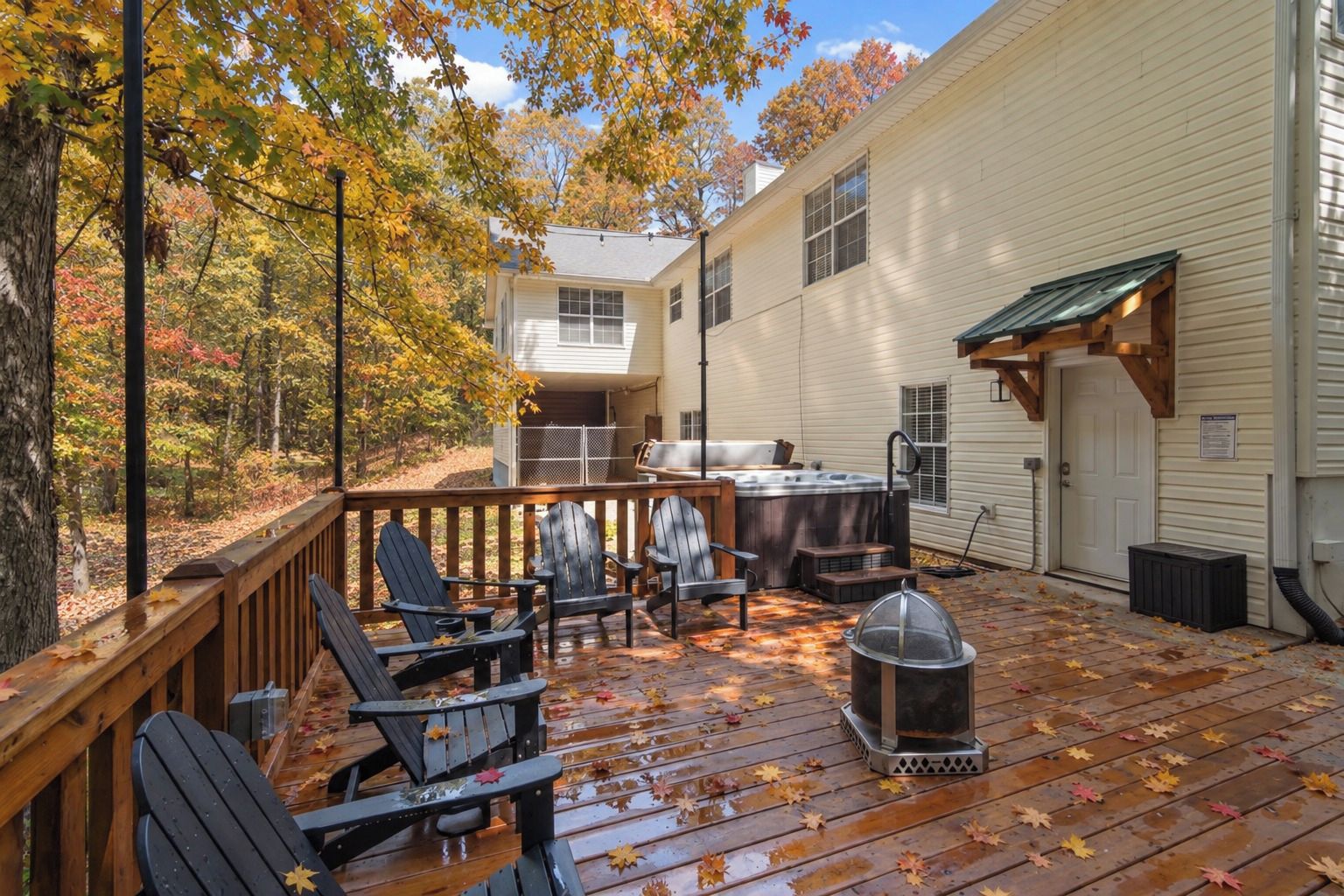 A wooden deck with Adirondack chairs, a hot tub, and a fire pit.