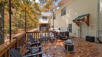 A wooden deck with Adirondack chairs, a hot tub, and a fire pit.